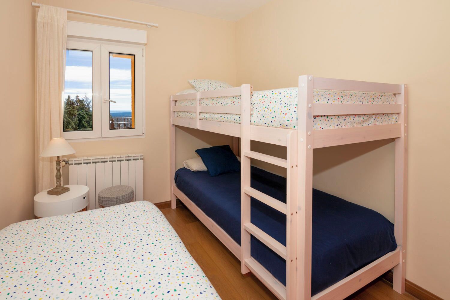 Une chambre avec des lits superposés, une fenêtre donnant sur un beau paysage, une lampe et un radiateur.
