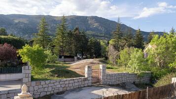 Un muro de piedra con una verja que da a una zona cubierta de hierba, con árboles y una montaña al fondo.