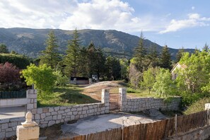 A stone wall with a gate leading to a grassy area with trees and a mountain in the background.