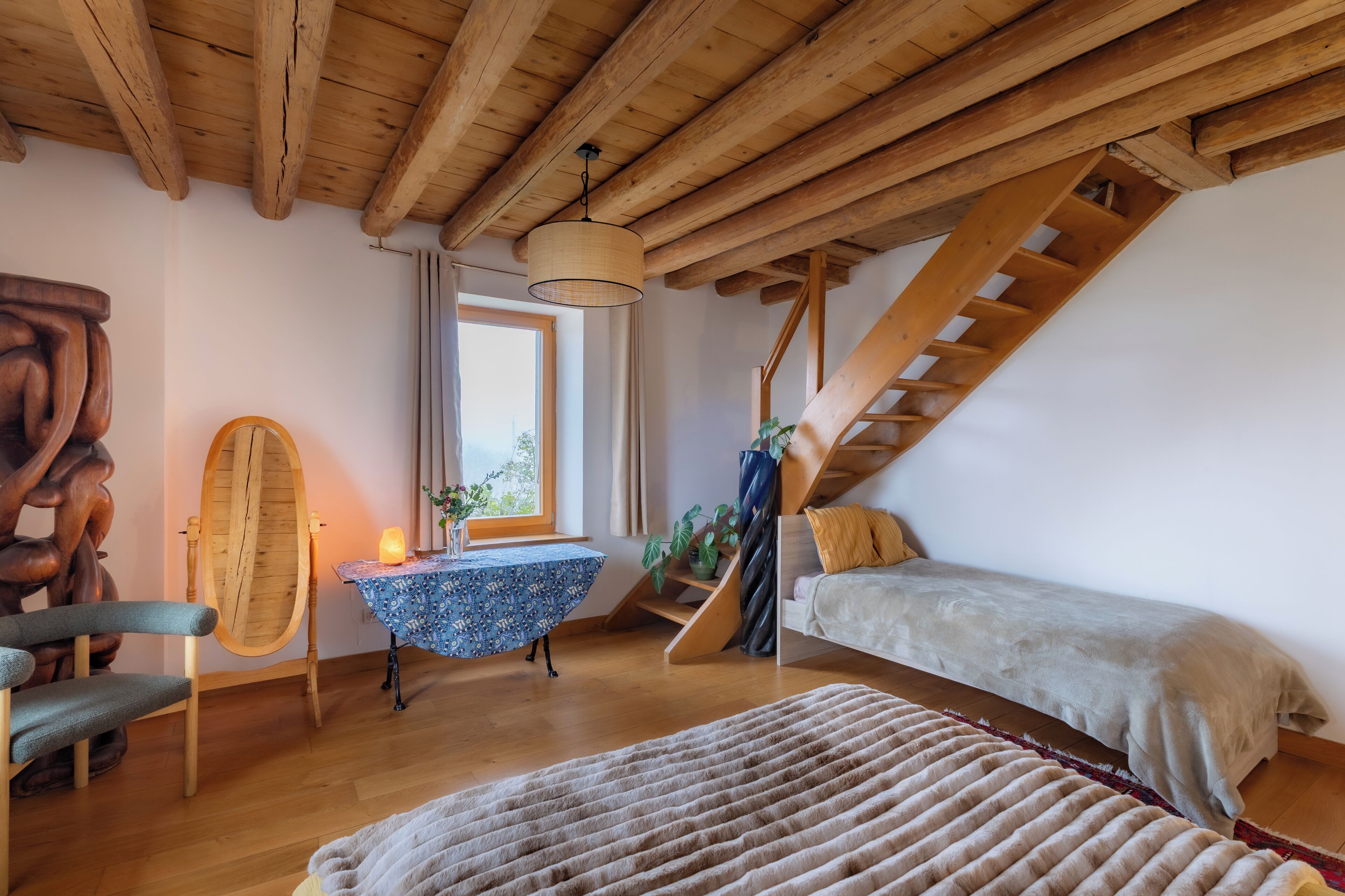 Une pièce chaleureuse avec un plafond en bois, un lit, une table avec une lampe et une fenêtre.