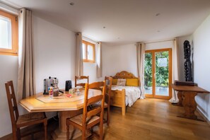 A room with a wooden dining table, chairs, a bed with a wooden headboard, a small table with a lamp, and a view through a glass door to the outside. - Vrbo Property (Neydens)