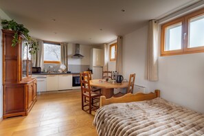 A cozy room with a bed, wooden furniture, a dining table, and a kitchen area. - Vrbo Property (Neydens)