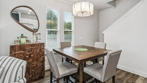 A dining area with a wooden table, four chairs, a chandelier, a mirror, and a cabinet with decorative carvings. - The Reverie - Downtown Pensacola - Convenient Corner Lot - Great For Business Travelers - Fast WiFi (Pensacola)