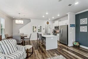 A modern kitchen with white cabinetry, a central island, and a dining area with a striped sofa. - The Reverie - Downtown Pensacola - Convenient Corner Lot - Great For Business Travelers - Fast WiFi (Pensacola)