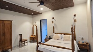 Quarto com uma cama de dossel, um ventilador de teto, um guarda-roupa de madeira, uma cadeira, uma mesinha de cabeceira e um criado-mudo.