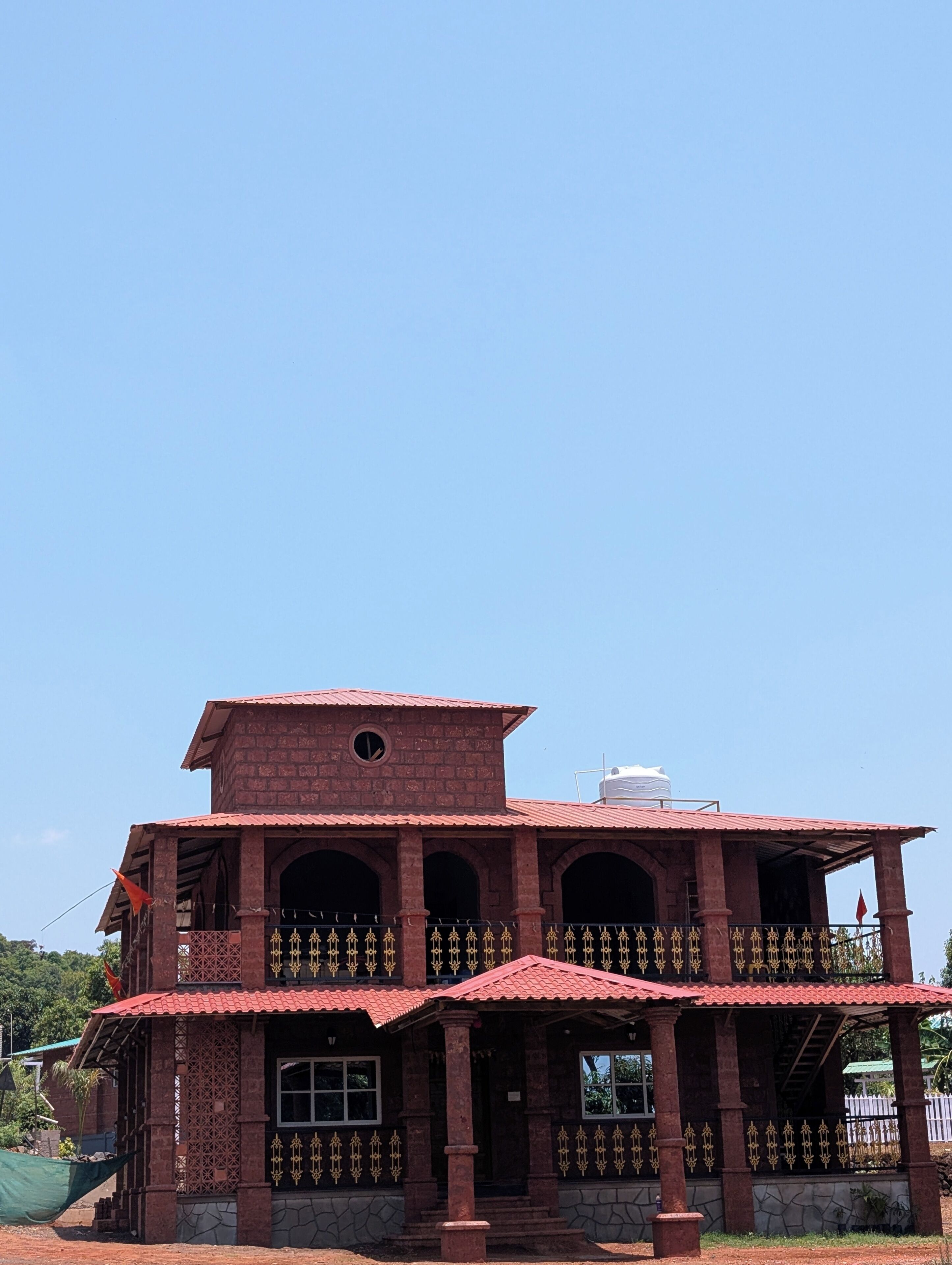 Um edifício de dois andares com telhado de telhas vermelhas, várias arcadas e uma varanda com grades decorativas.