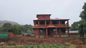 A two-story building with a balcony, surrounded by a vegetable garden.