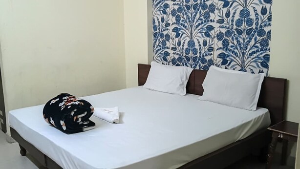 Habitación de hotel con cama, almohada, toalla doblada, puerta y cortina estampada.