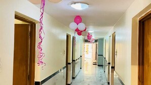 Un pasillo con suelo de mármol, puertas a ambos lados y globos colgando del techo.