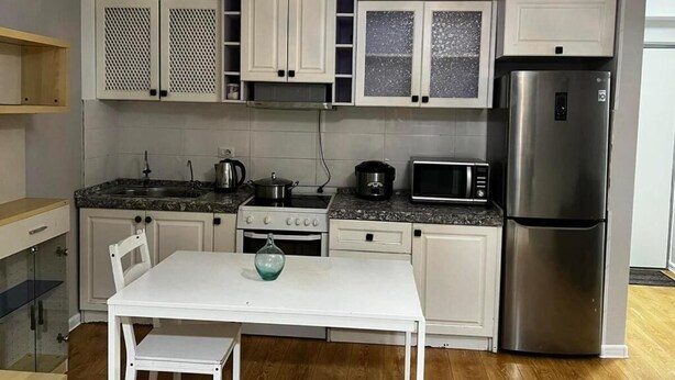 A compact kitchen with white cabinets, a stainless steel refrigerator, a microwave, and a gas stove.
