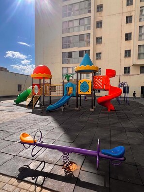 A playground with various play structures including slides and swings, set against a building with multiple windows. - Delightful 1-bedroom and 1 living room apartment near the city center in UB city (Ulaanbaatar)