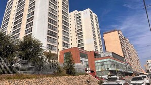 A high-rise building with multiple floors, a prominent logo on the facade, and a clear blue sky in the background.