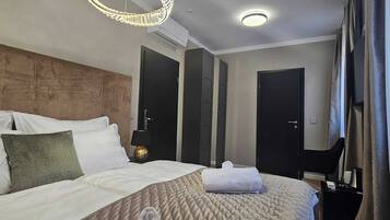 A hotel room with a large bed, a round ceiling light, a wall-mounted air conditioner, and a dark door.