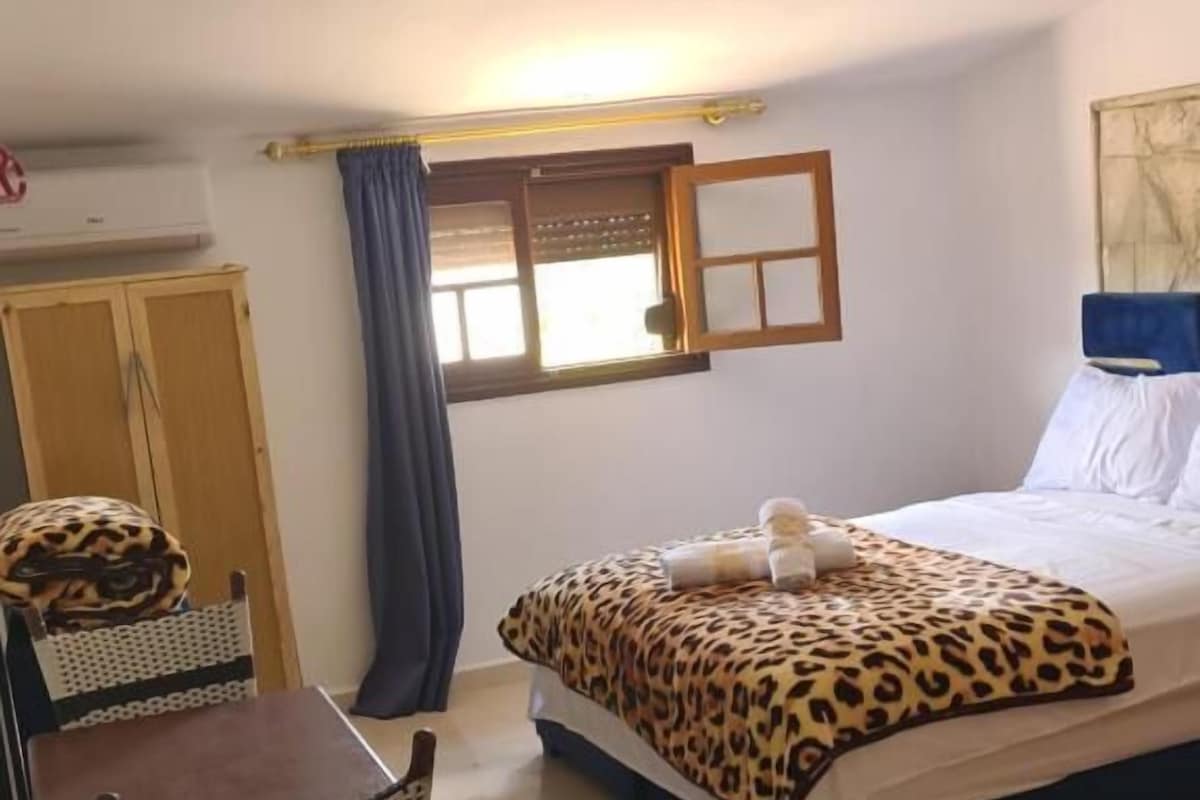 Een slaapkamer met een bed, een bureau, stoelen, een raam en een plafondventilator.