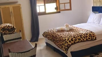 Une chambre à coucher avec un lit, un bureau, des chaises, une fenêtre et un ventilateur de plafond.