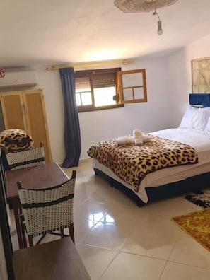 Een slaapkamer met een bed, een bureau, stoelen, een raam en een plafondventilator.