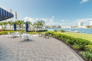 An outdoor patio with tables and chairs, a water body, and buildings in the background. - Park Shore-Luxury 3BR/3BA condo on Venetian Bay-boat slip, carport, private Park Shore beach pass (Naples)