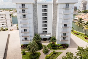 A multi-story hotel with balconies, a central entrance, and a landscaped courtyard with palm trees. - Park Shore-Luxury 3BR/3BA condo on Venetian Bay-boat slip, carport, private Park Shore beach pass (Naples)