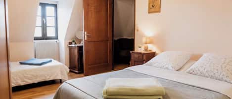 Ein Schlafzimmer mit einem großen Bett, einem kleineren Bett, einem Holzschrank, einem Nachttisch mit Lampe und einem Fenster mit Blick.