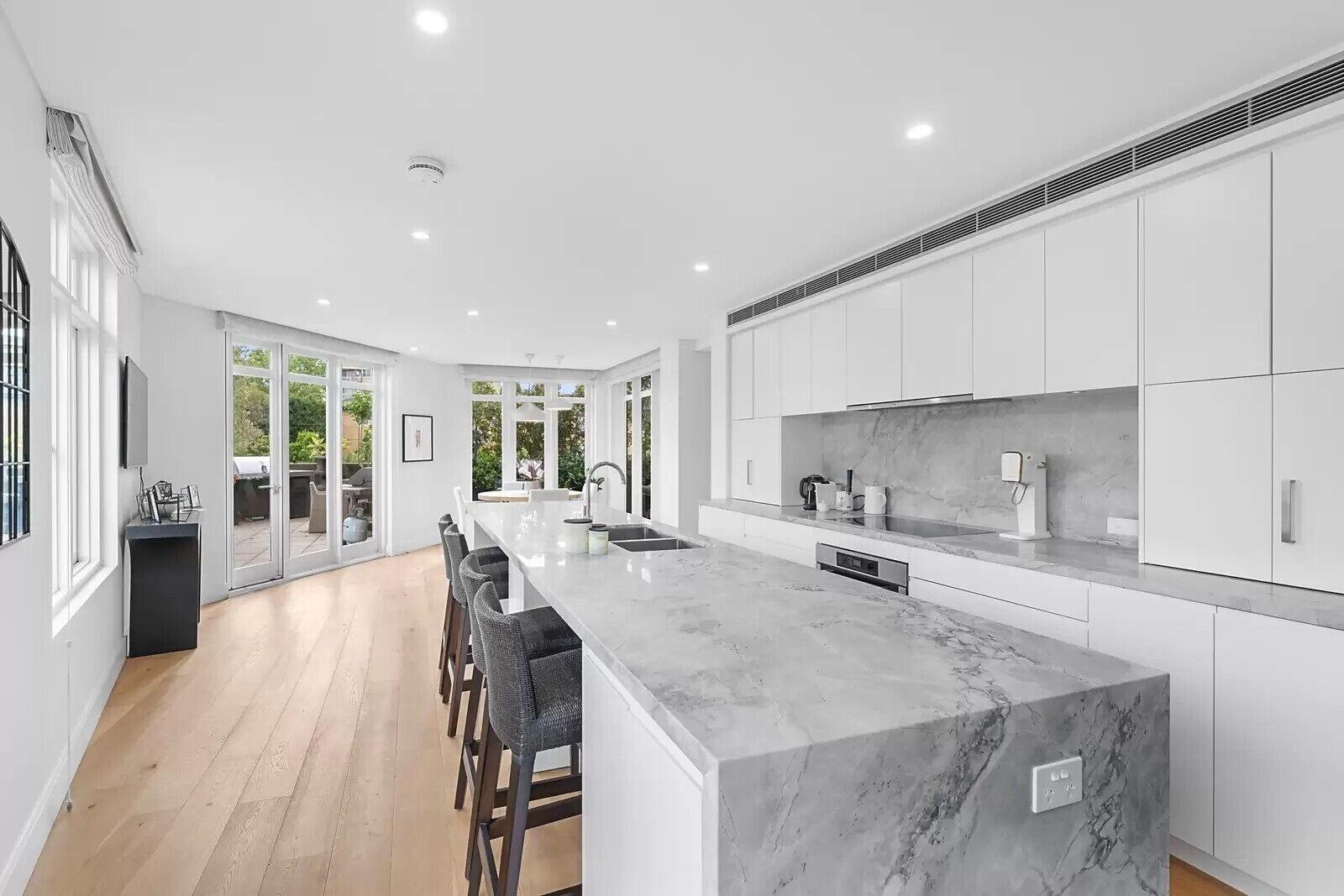 A modern kitchen with a marble countertop, white cabinetry, and a long island with bar stools.