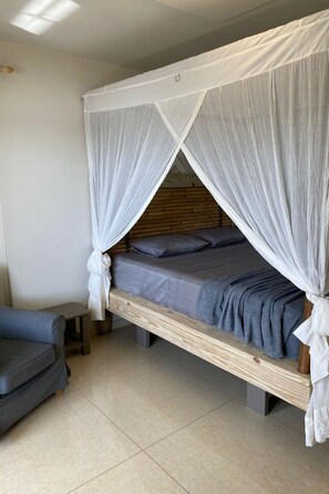 A single bed with a wooden frame and a canopy, a small bedside table, and a grey sofa in a room with tiled flooring. - Villa del Mare - Waterfront Villa by Interhome (Willemstad)