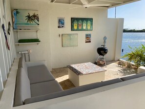 A covered outdoor seating area with a grill, artwork, and a view of the water. - Villa del Mare - Waterfront Villa by Interhome (Willemstad)