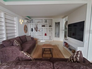 A living room with a brown sofa, a coffee table, and a TV on the wall. - Villa del Mare - Waterfront Villa by Interhome (Willemstad)