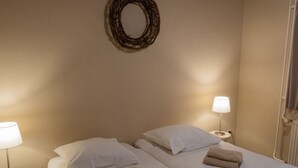 Una camera d'albergo con due letti, ciascuno con un cuscino e un asciugamano piegato. Sopra i letti si trova uno specchio fissato alla parete e una lampada su ogni lato della stanza.