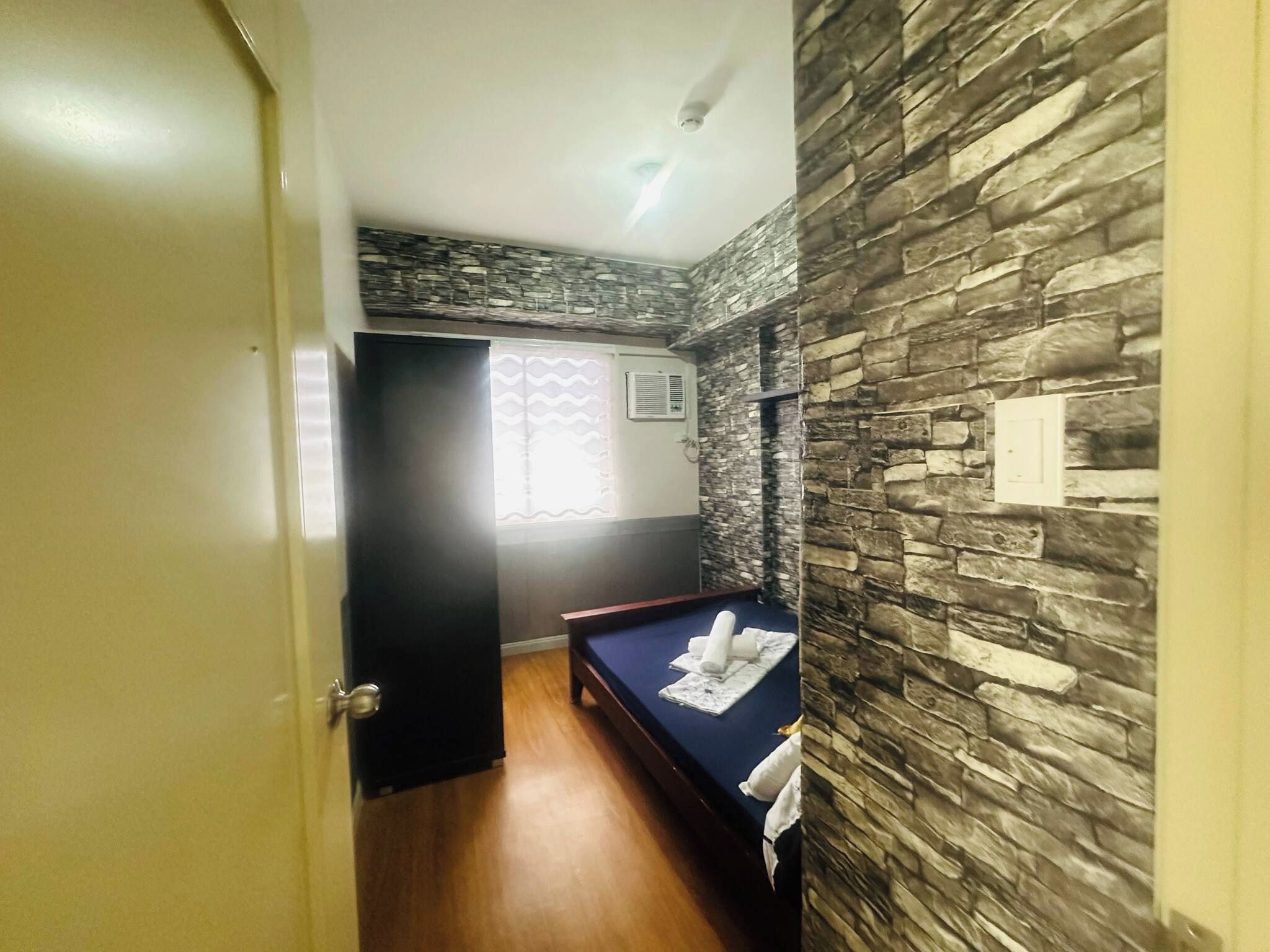 Una habitación de hotel con una cama, suelo de madera, pared de piedra y una puerta.