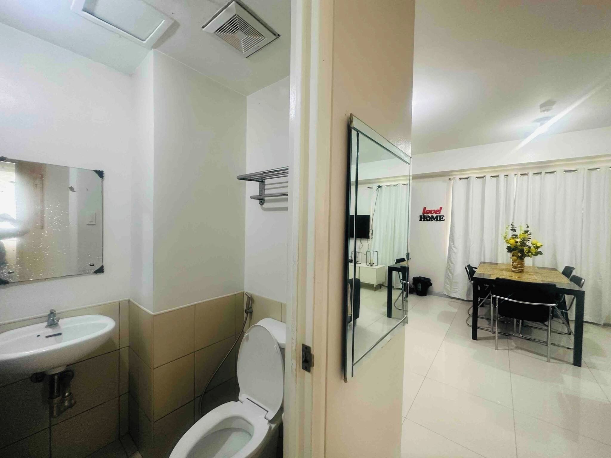 Un baño moderno con lavamanos, inodoro y espejo. Junto a él, un comedor con mesa y sillas, y un letrero que dice 'love! HOME'.