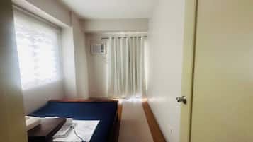 Una habitación con una cama, una mesita de noche con una lámpara, una ventana con cortinas y una puerta.