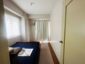 Una habitación con una cama, una mesita de noche con una lámpara, una ventana con cortinas y una puerta.