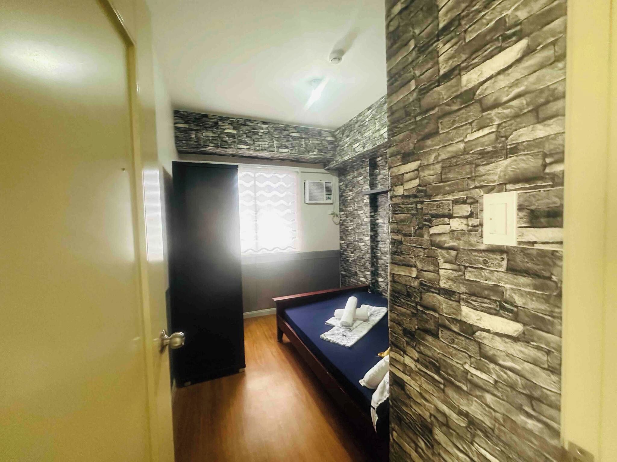 Habitación de hotel con cama, suelo de madera, pared de piedra y una puerta.