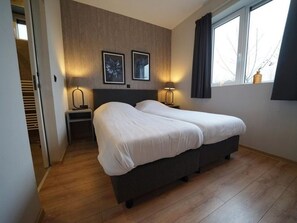 Ein Schlafzimmer mit einem Doppelbett, zwei Nachttischen mit Lampen, einem Fenster mit Vorhängen und einem Holzboden.