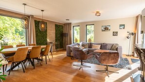 A modern living room with a dining area, large windows, and a green wall. - Vakantiepark De Wiltzangh - De Havezate Wellness by Interhome (Ruinen)