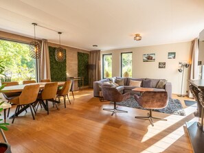 A modern living room with a dining area, large windows, and a green wall. - Vakantiepark De Wiltzangh - De Havezate Wellness by Interhome (Ruinen)