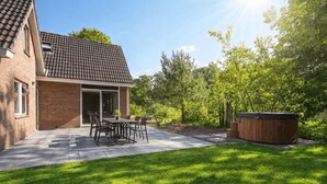 A brick house with a tiled roof, a patio with a table and chairs, and a hot tub in the yard. - Vakantiepark De Wiltzangh - De Havezate Wellness by Interhome (Ruinen)