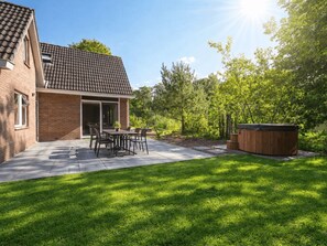 A brick house with a tiled roof, a patio with a table and chairs, and a hot tub in the yard. - Vakantiepark De Wiltzangh - De Havezate Wellness by Interhome (Ruinen)