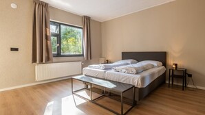A modern bedroom with a large bed, a bedside table, a bench, and a window with curtains. - Vakantiepark De Wiltzangh - De Havezate Wellness by Interhome (Ruinen)