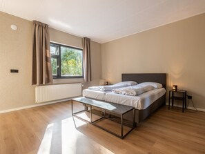 A modern bedroom with a large bed, a bedside table, a bench, and a window with curtains. - Vakantiepark De Wiltzangh - De Havezate Wellness by Interhome (Ruinen)