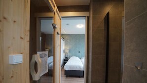 Hotellihuone, jossa on puinen ovi, sänky, yöpöytä ja pieni sivupöytä.