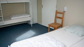 Asuntolan huone, jossa on kerrossängyt, yksi erillinen sänky, puinen tuoli ja yöpöytä.