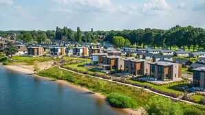 A residential area with modern houses by a river, featuring a mix of single and multi-story buildings, well-maintained lawns, and a clear sky. - Vakantiepark Aan de Maas - Maas Lande | 4p by Interhome (Kerkdriel)