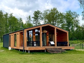 A modern wooden cabin with a covered porch, large windows, and a dining area.