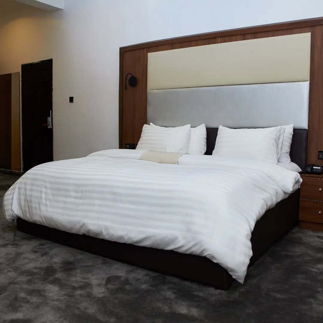 A hotel room with a large bed, a wooden headboard, and a dark floor.