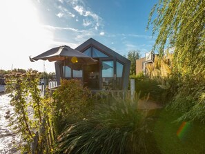 Ein modernes Haus mit Glasfassade, einer Terrasse und Blick auf das Wasser.