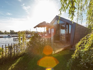 Ein modernes Haus mit Glastür, Holzterrasse und Blick auf das Wasser.