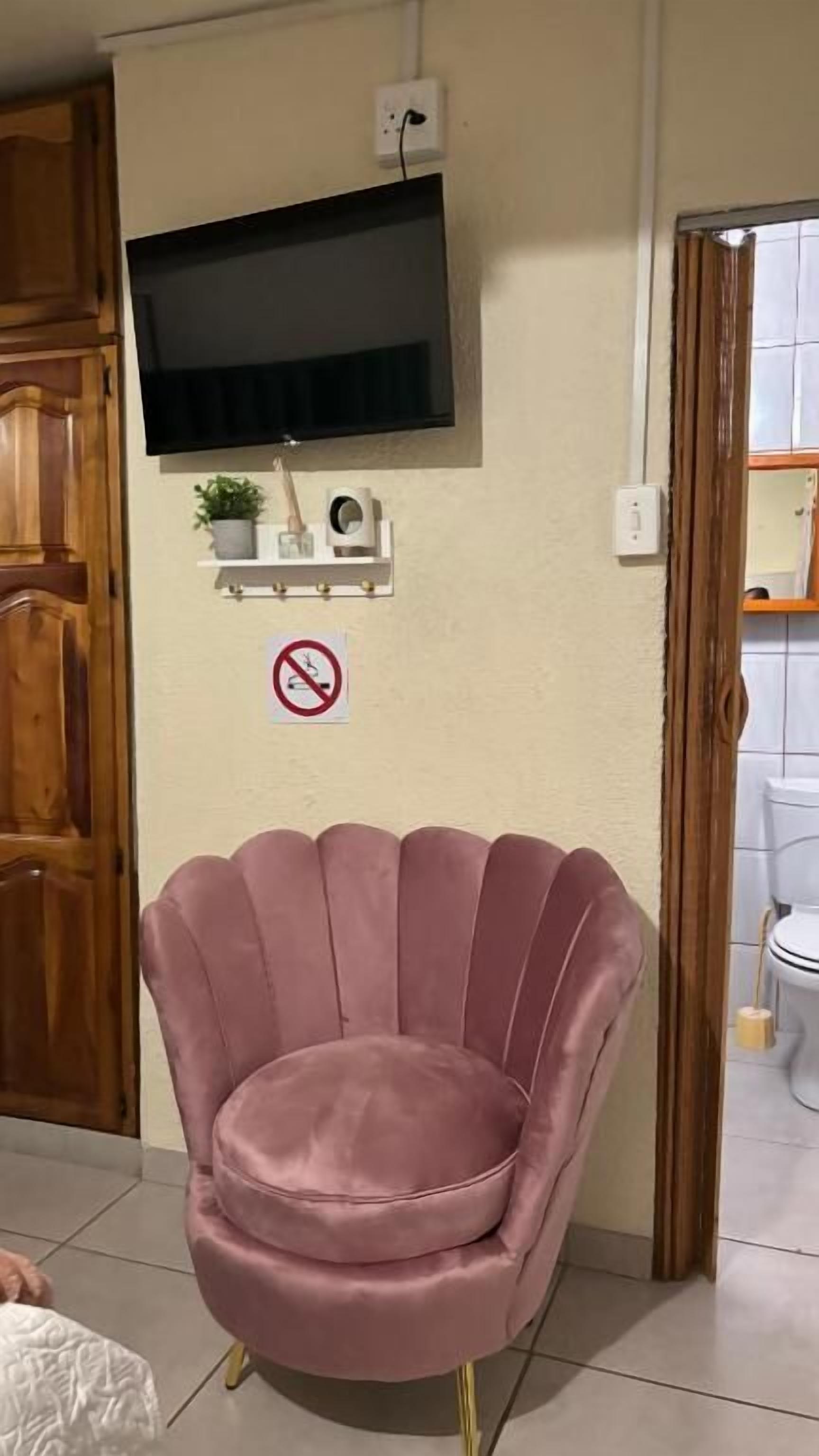 A room with a television mounted on the wall, a pink chair, and a no-smoking sign.