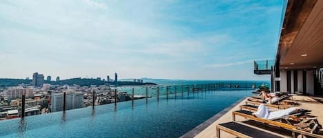 Piscina infinita no terraço com vista para a cidade, espreguiçadeiras e um deck de madeira.