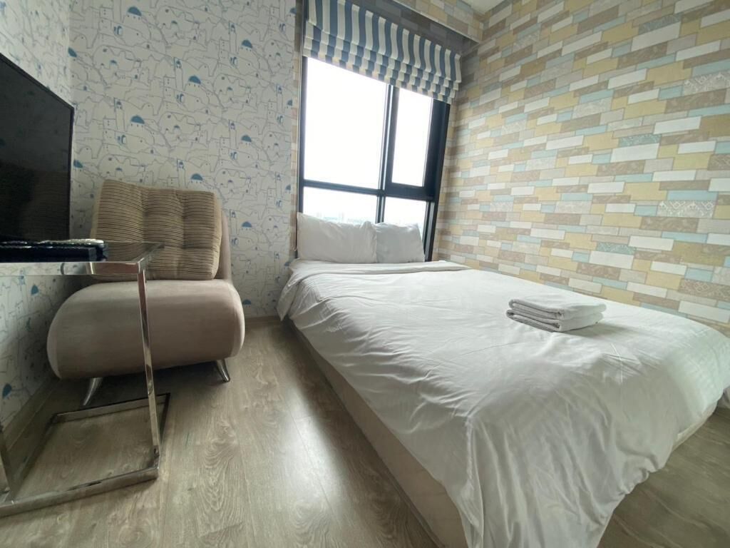 A hotel room with a bed, a chair, a television, and a window with a striped curtain.